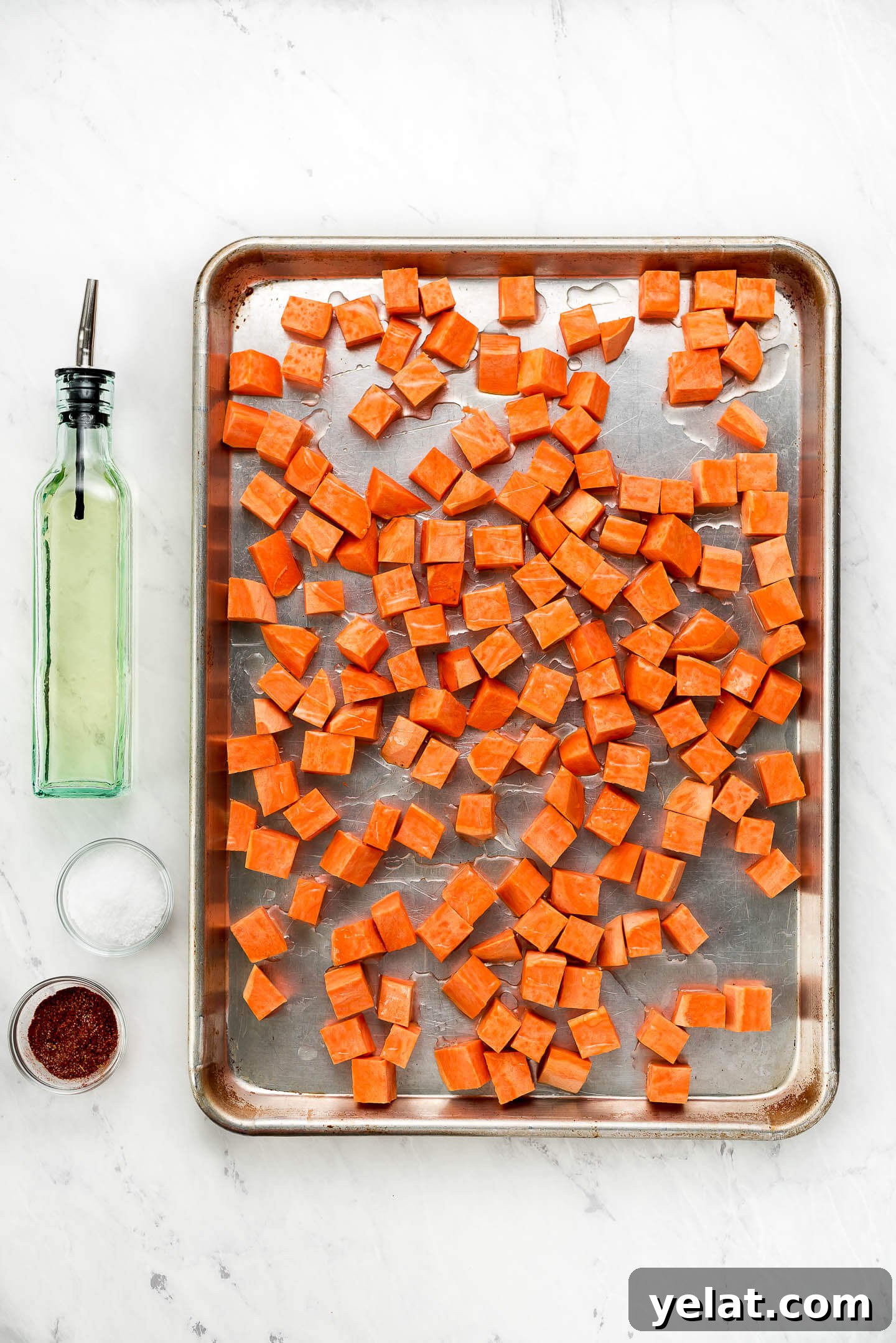 Crispy Roasted Sweet Potatoes with Garlic and Herbs 4 Cubed raw sweet potatoes on a baking sheet drizzled with olive oil and seasonings in small bowls to the side.