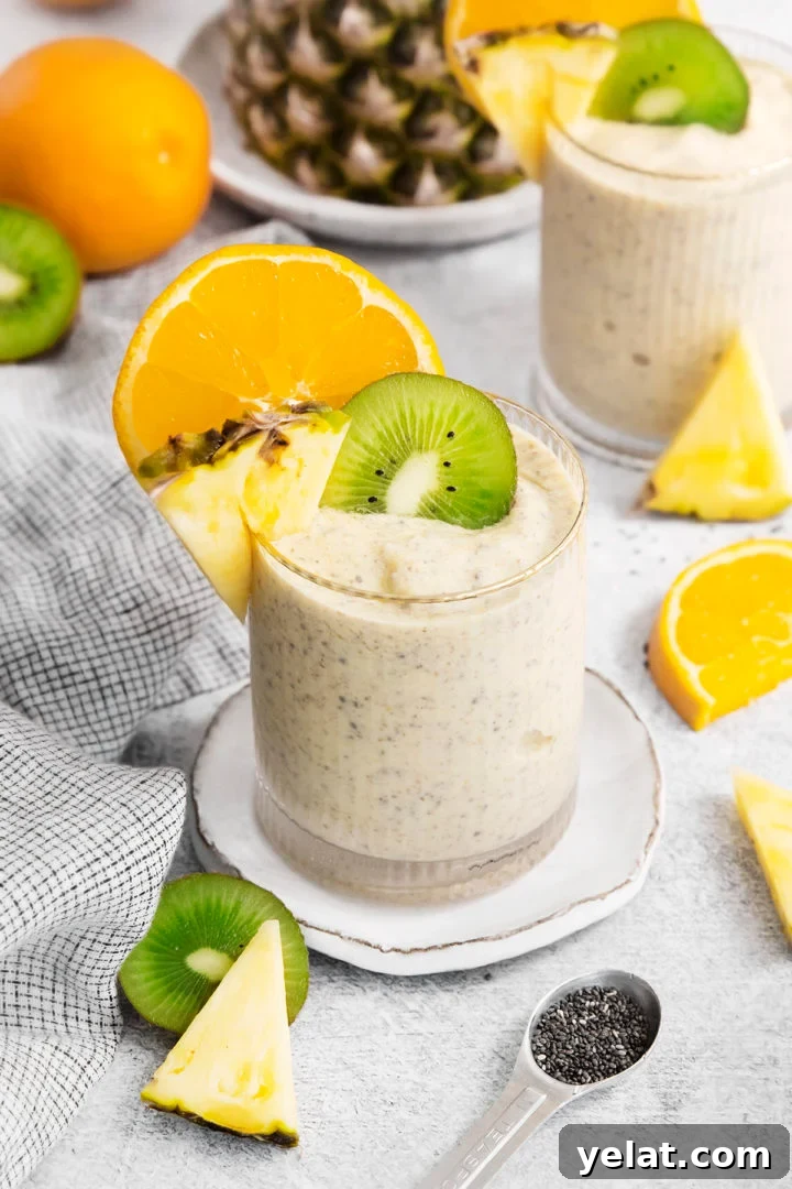 pineapple orange smoothie in two glasses surrounded by fresh pineapple, oranges, and kiwi