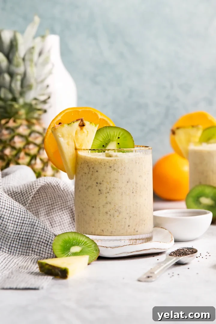 glass filled with a pineapple orange smoothie garnished with fresh orange, pineapple, and kiwi