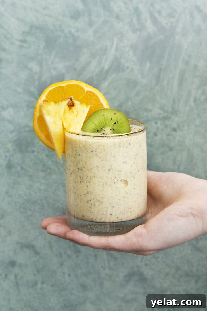 woman holding a glass of a pineapple orange smoothie against a teal background