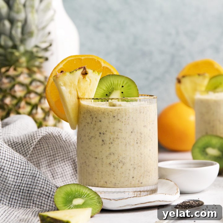 glass filled with a pineapple orange smoothie garnished with fresh orange, pineapple, and kiwi