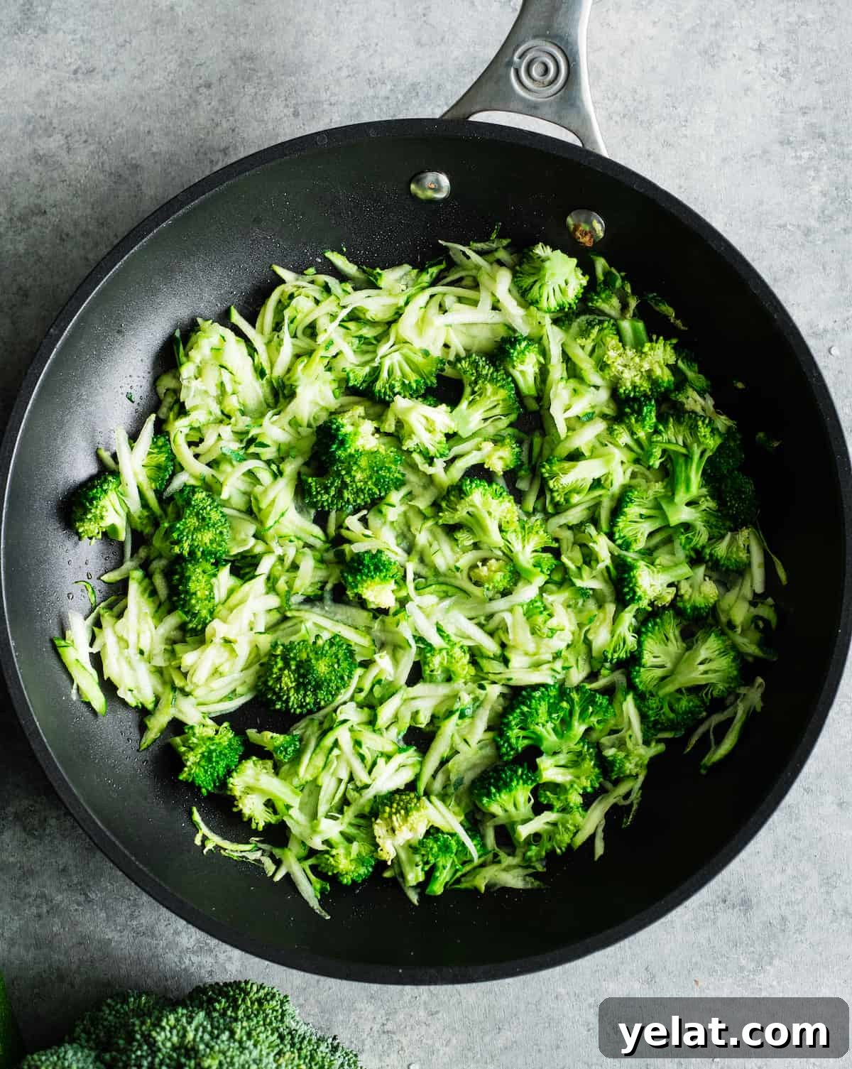 overhead view of shredded zucchini & broccoli cooking in a pan to make vegetable mac and cheese