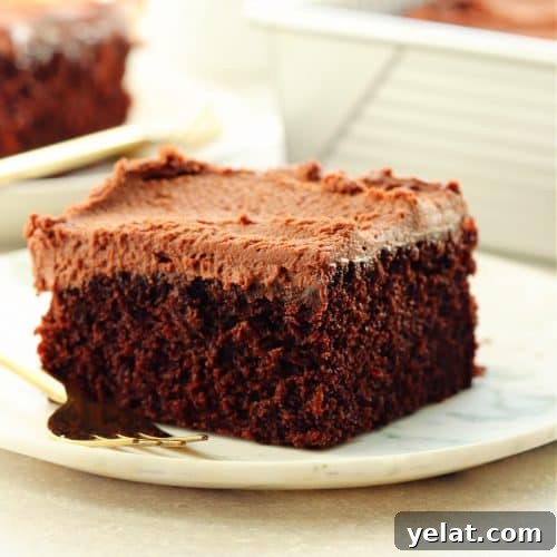 Square image of a serving of eggless chocolate cake with frosting on a white marble plate.