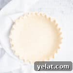 Overhead view of unbaked pie crust in a white pie pan with crimped edges.