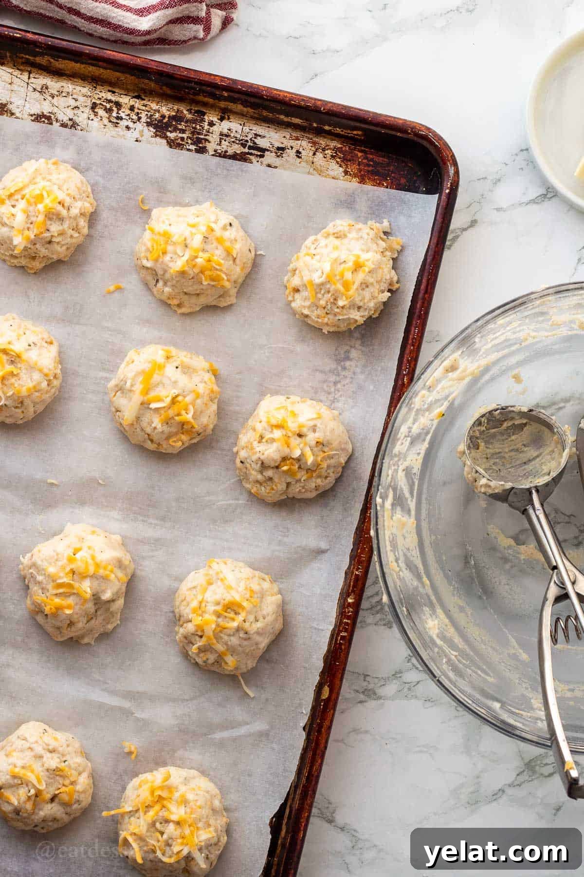 Garlic Cheddar Drop Biscuits Recipe: Quick Savory Biscuits 8 Raw garlic cheese biscuit dough balls on parchment paper on metal baking sheet.