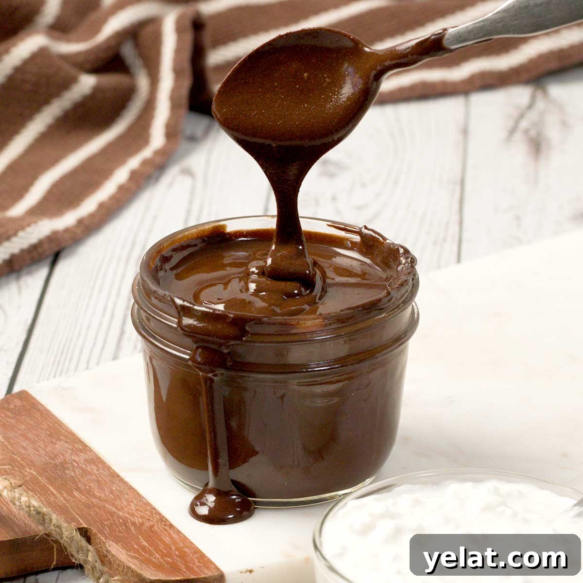 Light Protein Cottage Cheese with Chocolate Sauce Recipe 2 A close-up of a spoon dripping protein cottage cheese chocolate sauce in a mason jar on a white cutting board.