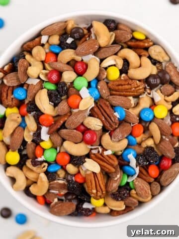A white bowl filled with homemade trail mix, featuring nuts, raisins, and M&M's.