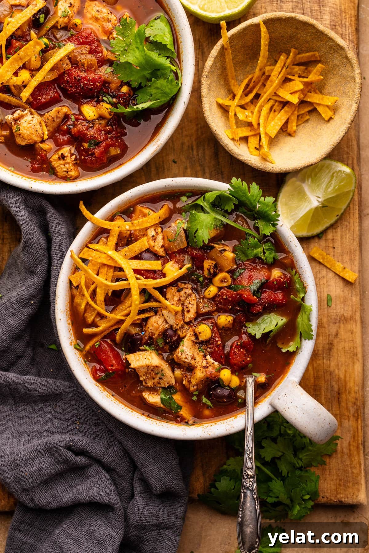 Hearty Chicken Taco Soup Recipe for Cozy Weeknight Dinners 2 Two white bowls with chicken taco soup in it. The two bowls are arranged on a wooden board with tortilla strips, lime slices, and a gray napkin placed around the bowl.