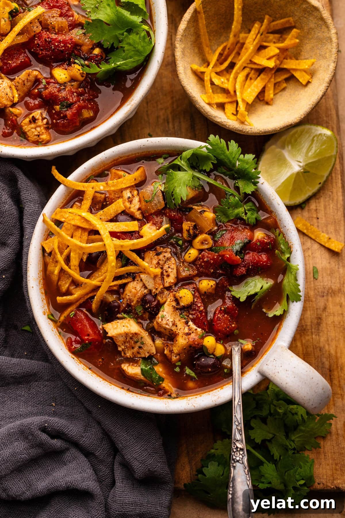 Hearty Chicken Taco Soup Recipe for Cozy Weeknight Dinners 6 A white bowl with chicken taco soup in it. The board is arranged on a wooden board with tortilla strips, lime slices, and a gray napkin placed around the bowl.