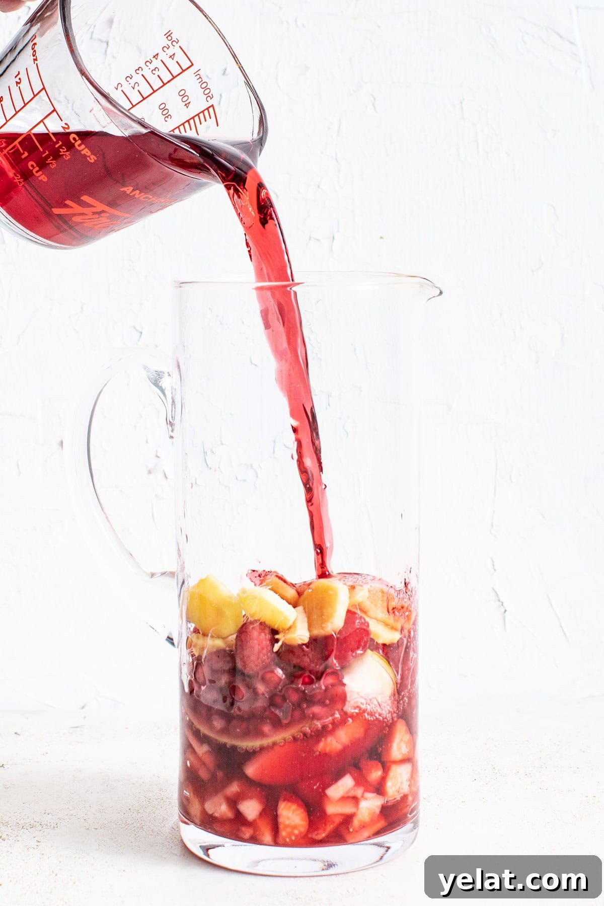 Pomegranate Virgin Sangria Recipe — Refreshing Party Drink 5 Pouring pomegranate juice into a tall pitcher with fresh fruit.