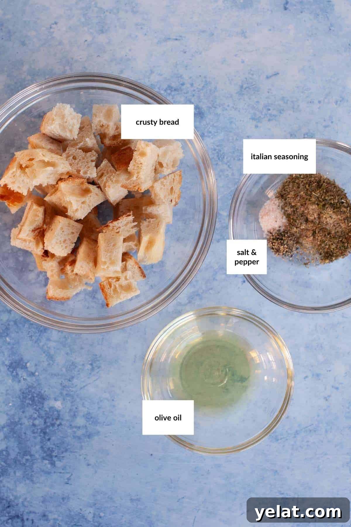 Crispy Homemade Croutons: Simple Recipe for Perfect Salads 3 Three bowls contain cubed crusty bread, a mix of Italian seasoning with salt and pepper, and olive oil, all labeled—perfect ingredients for homemade croutons. The background is a light blue surface.