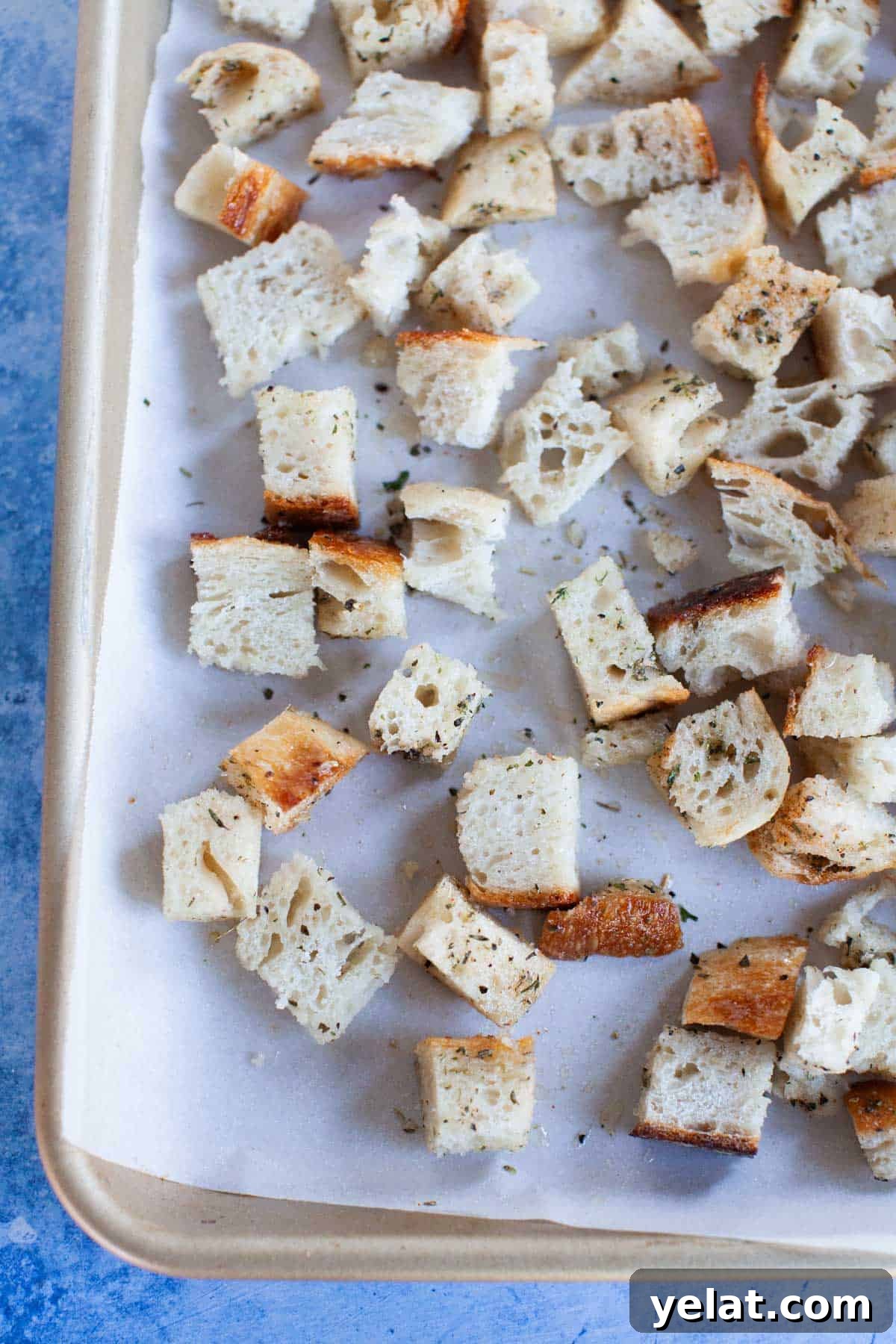Crispy Homemade Croutons: Simple Recipe for Perfect Salads 8 Seasoned and oiled sourdough pieces laid out on a parchment-paper lined baking sheet.
