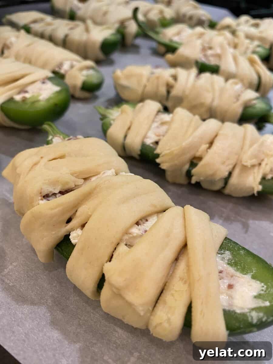 Jalapeño Bacon Mummies: Spicy Stuffed Appetizer for Parties 3 Unbaked jalapeño halves wrapped in crescent dough on a baking sheet.