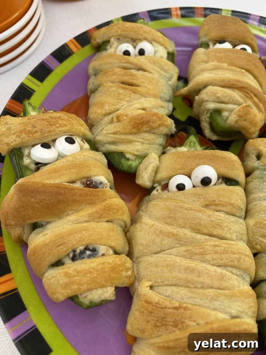 Jalapeño Bacon Mummies: Spicy Stuffed Appetizer for Parties 6 Jalapeño popper wrapped with dough and displaying candy eyes.