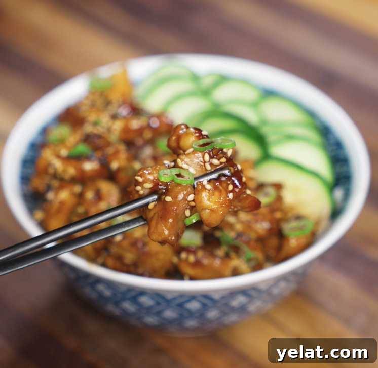 Garlic Butter Chicken Recipe with Crispy Pan-Seared Thighs 3 A pair of chopsticks holds up a glistening piece of garlic butter chicken garnished with scallions and sesame seeds, highlighting the caramelized sauce.