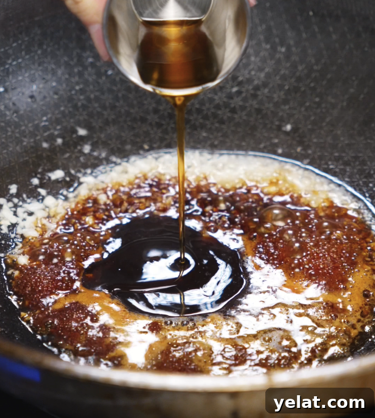 Garlic Butter Chicken Recipe with Crispy Pan-Seared Thighs 7 A stream of soy-based sauce is poured into a pan of sautéed garlic and butter to create a sweet, savory glaze for the chicken.