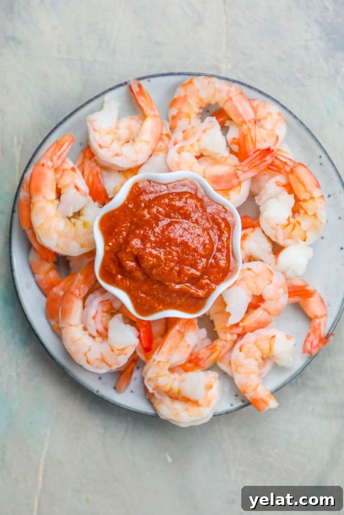 cooked shrimp cocktail on a plate around a cup of bright red cocktail sauce