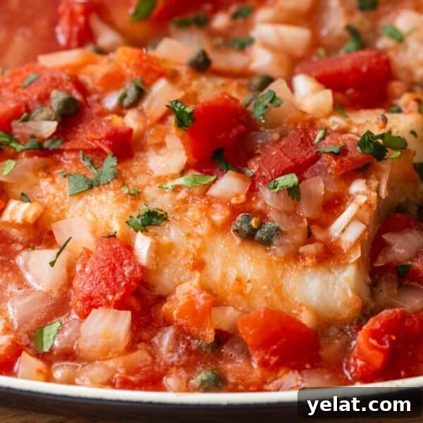 Close-up of easy Tuscan baked fish fillet topped with diced tomatoes, onions, capers, and chopped herbs.
