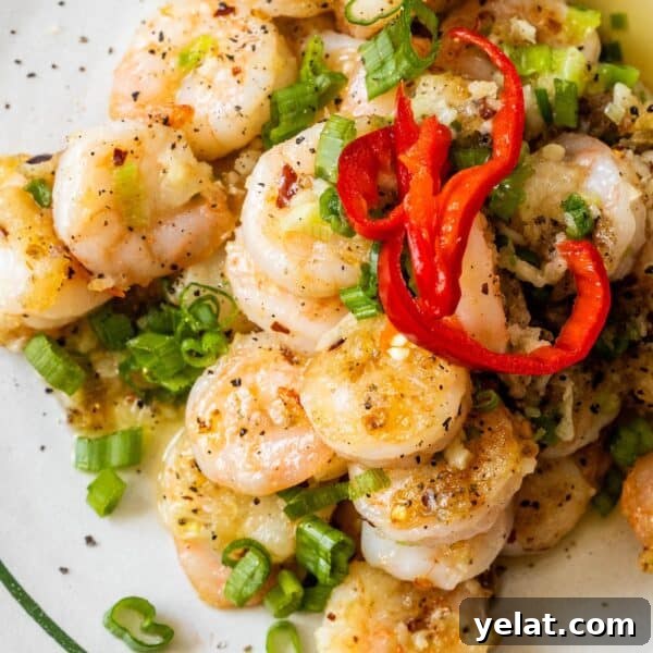 Salt and pepper shrimp cooked to perfection, garnished with sliced green onions, red chili peppers, and ground black pepper on a plate.