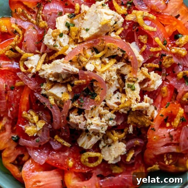 Close-up of a Tomato Salad featuring slices of tomatoes topped with shredded cooked chicken, caramelized onions, and crispy fried onions.