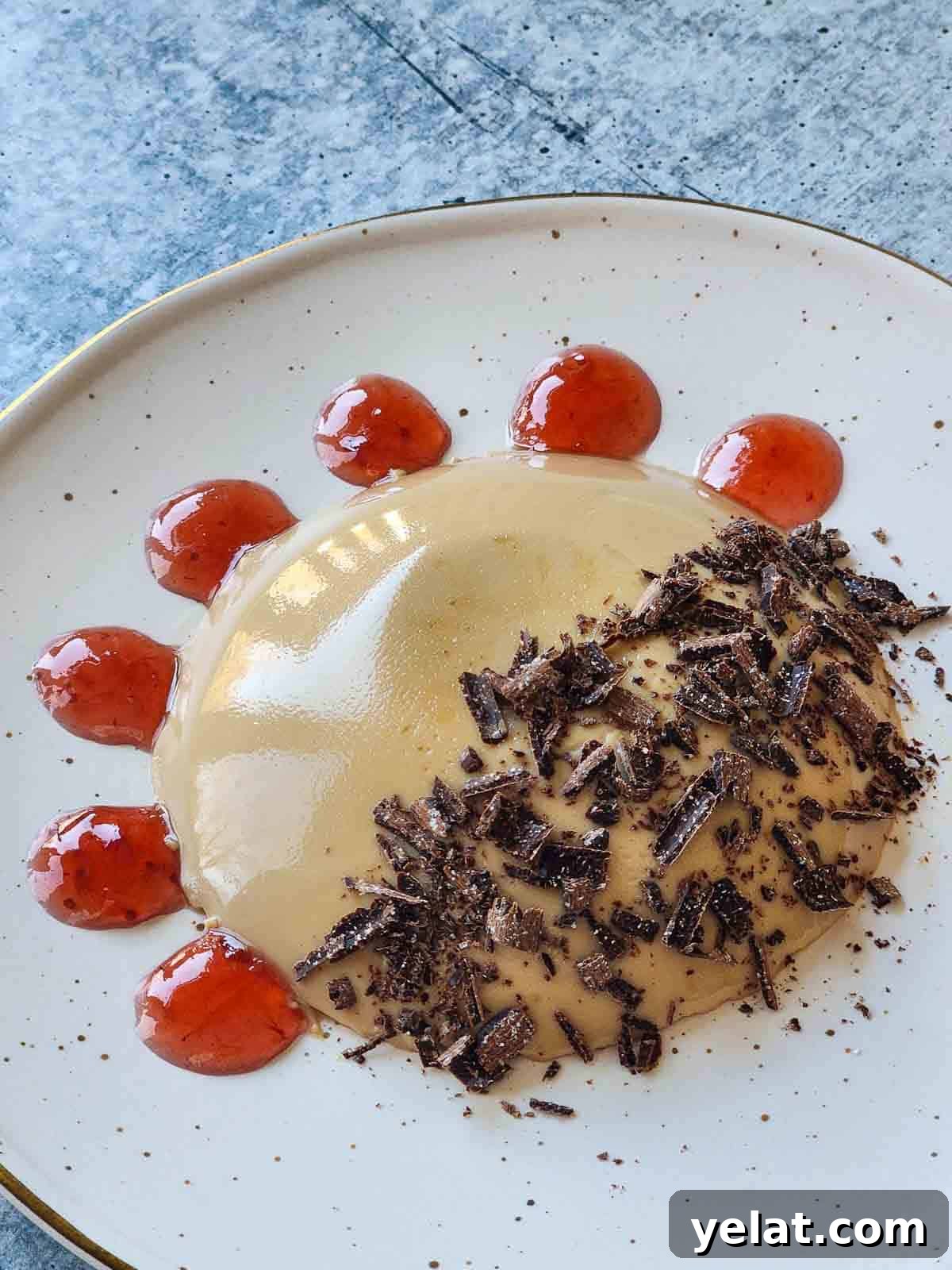 Panna cotta on a beige plate with raspberry swirls and shaved chocolate.