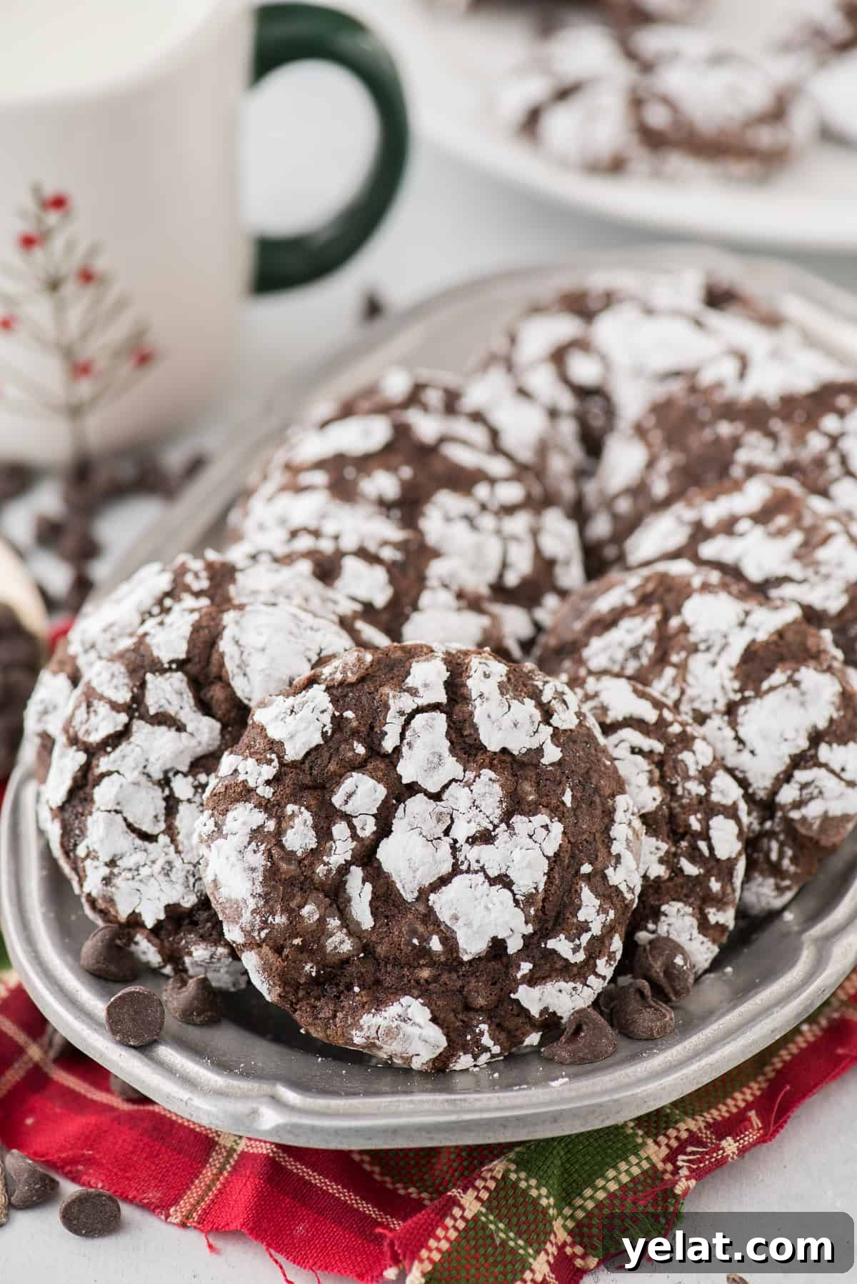 Chewy Chocolate Crinkle Cookies Recipe for Perfectly Soft Centers 2 chocolate crinkle cookies rolled in powdered sugar on metal tray with red towel underneath