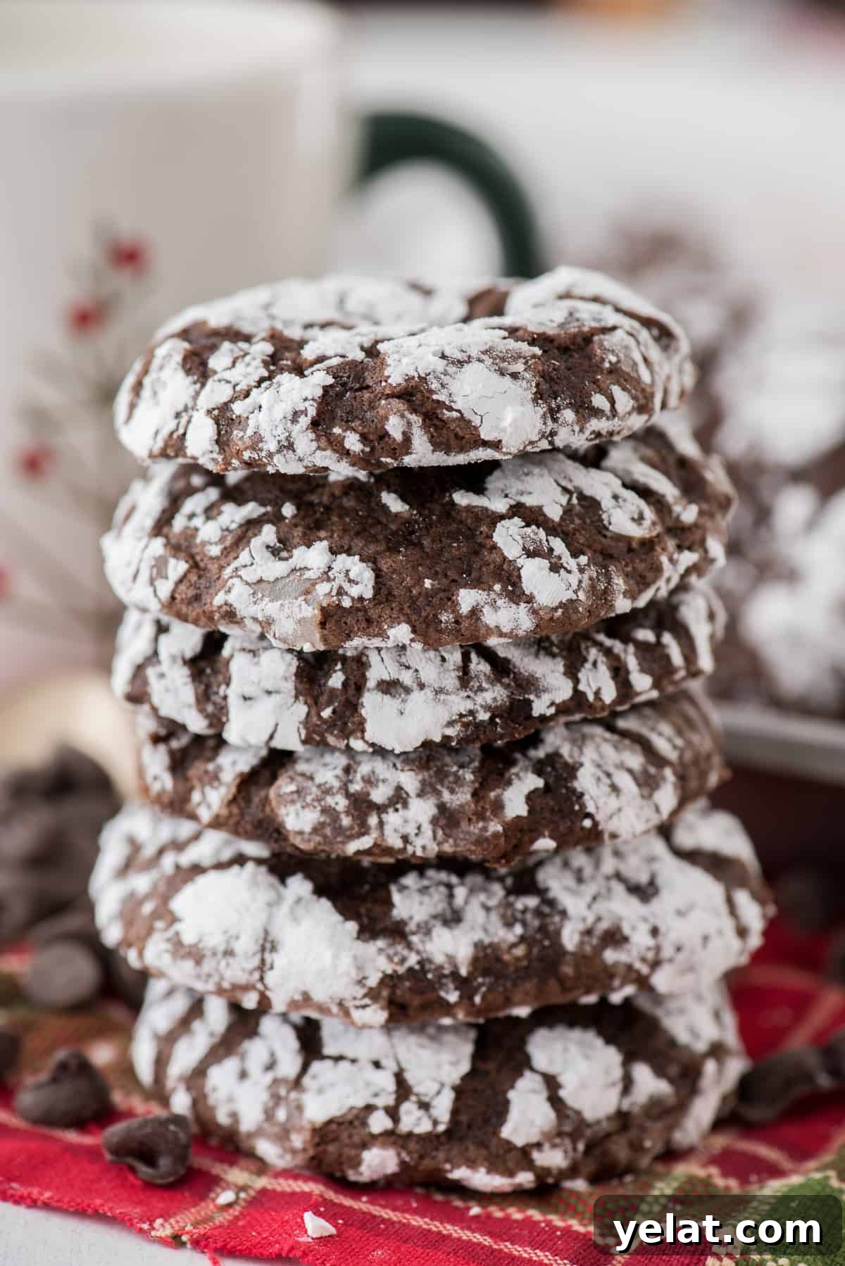 Chewy Chocolate Crinkle Cookies Recipe for Perfectly Soft Centers 3 chocolate crinkle cookies rolled in powdered sugar stacked on a red towel