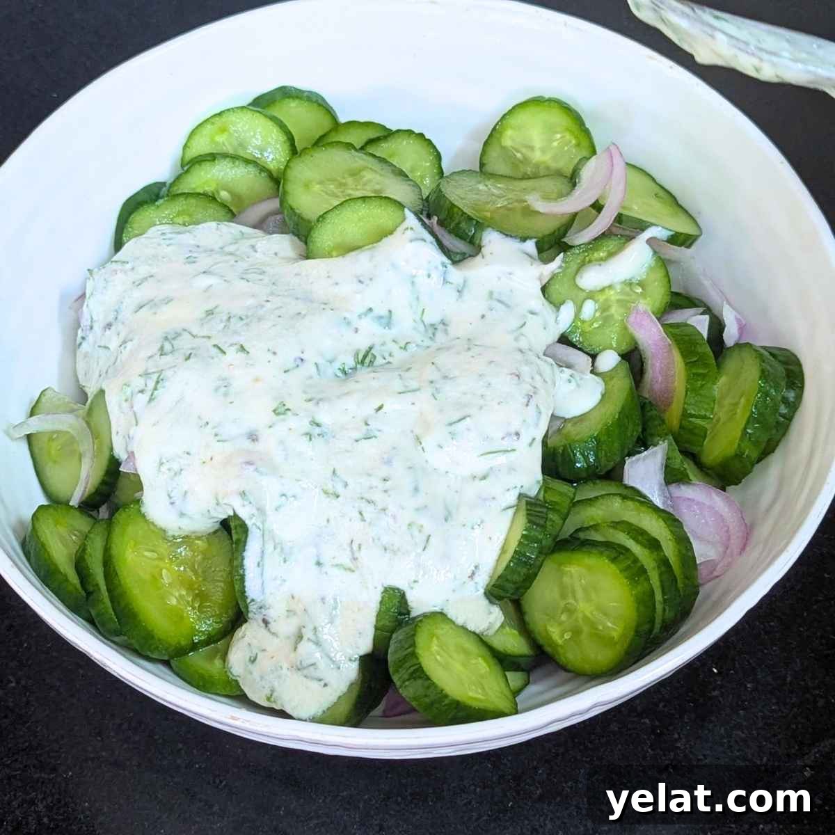 Creamy dressing poured on top of sliced cucumber and onion.