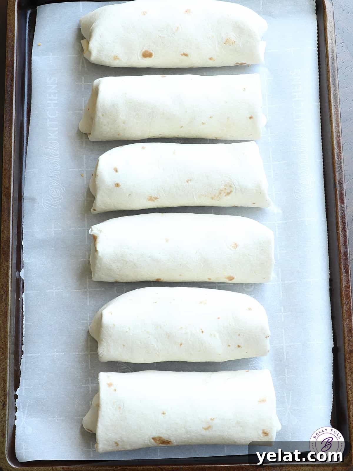 burritos in a row on parchment paper lined baking sheet