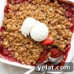 Top view of a pan of strawberry crisp with two spoons sticking out and a scoop of ice cream on top.
