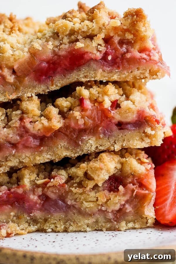 A stack of three strawberry rhubarb bars on a plate with two fresh strawberries next to them.