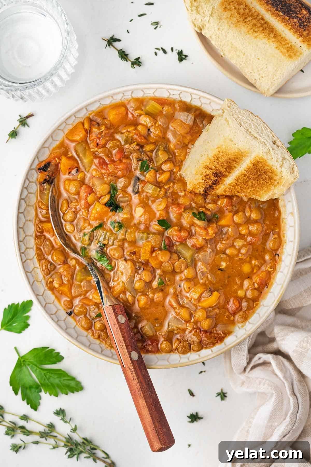Overhead view of a bowl of slow cooker lentil soup with a piece of bread and spoon stuck into it.
