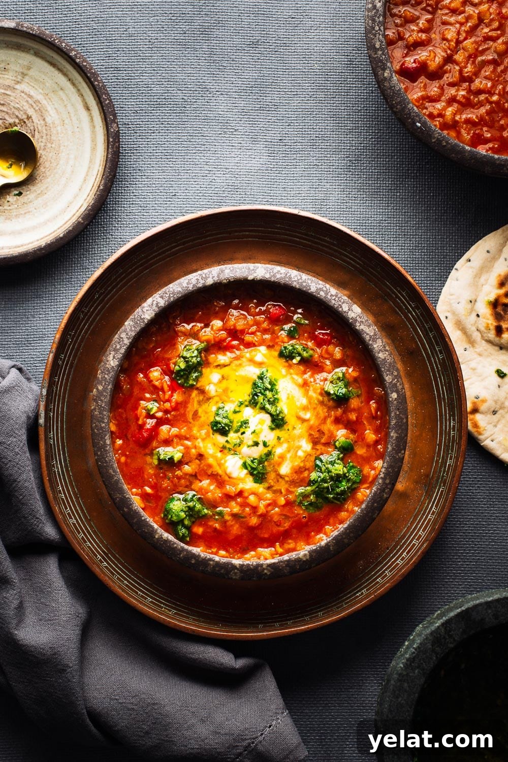 Bowls of bright red lentil soup viewed from above on a dark grey background.