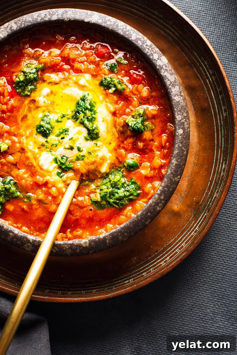 A bowl of red lentil soup with yoghurt and green chilli salsa and a gold spoon.
