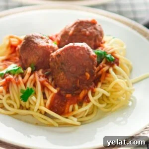 Spaghetti topped with gluten free air fryer meatballs, marinara sauce, and parsley on a white plate with a silver rim.