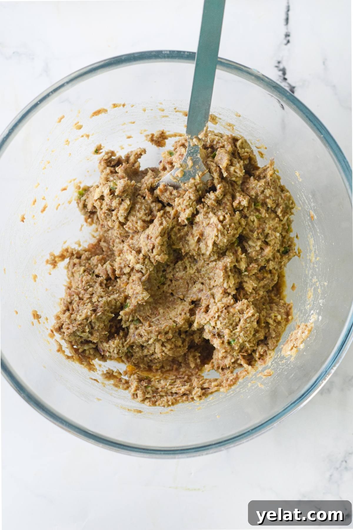 Air Fryer Meatballs in Marinara Sauce: Quick Homemade Recipe 15 A glass bowl with a mixture of raw vegan meatball recipe ingredients and a fork sits on a marble surface, ready to be transformed into delicious vegan meatballs with spaghetti marinara.