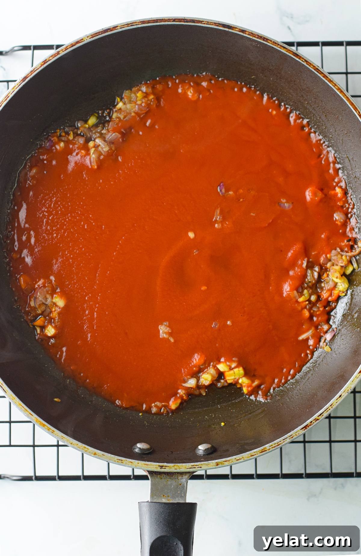 Air Fryer Meatballs in Marinara Sauce: Quick Homemade Recipe 19 A frying pan with tomato sauce and sautéed onions, perfect for preparing vegan meatballs with spaghetti marinara, rests on a cooling rack.