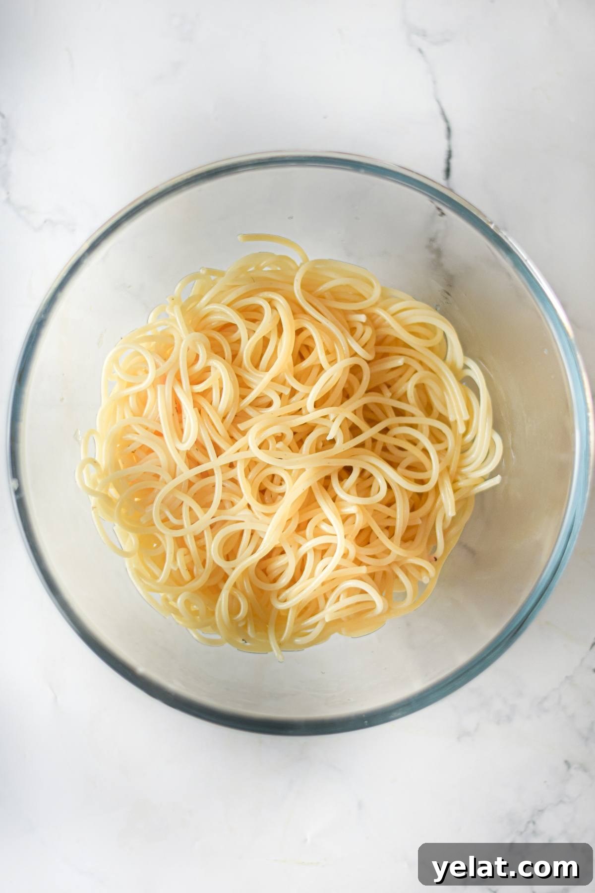 Air Fryer Meatballs in Marinara Sauce: Quick Homemade Recipe 20 A clear glass bowl filled with plain cooked spaghetti noodles on a white marble surface, ready to be paired with your favorite easy vegan meatballs.