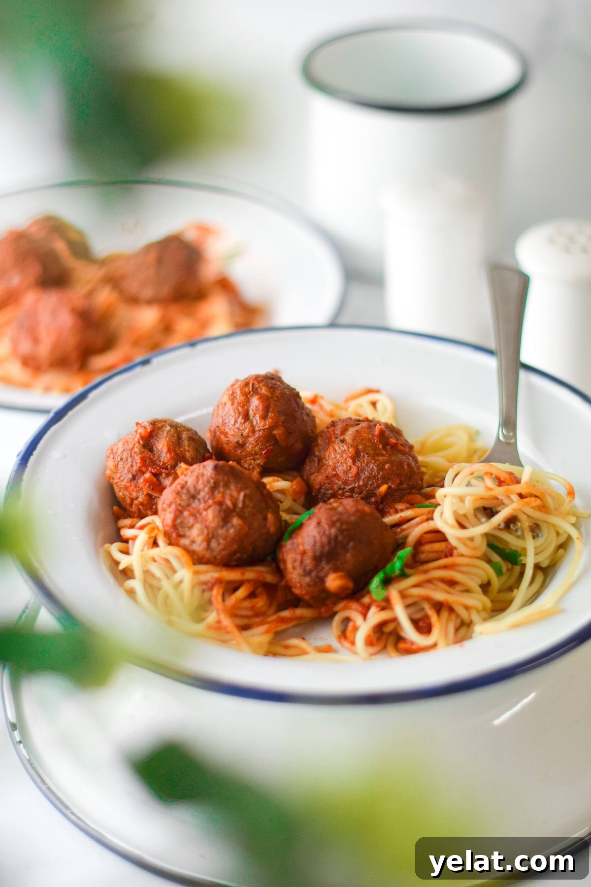 Air Fryer Meatballs in Marinara Sauce: Quick Homemade Recipe 6 A bowl of spaghetti with rich tomato sauce and vegan meatballs with spaghetti marinara, accompanied by a fork and a blurred plate in the background.