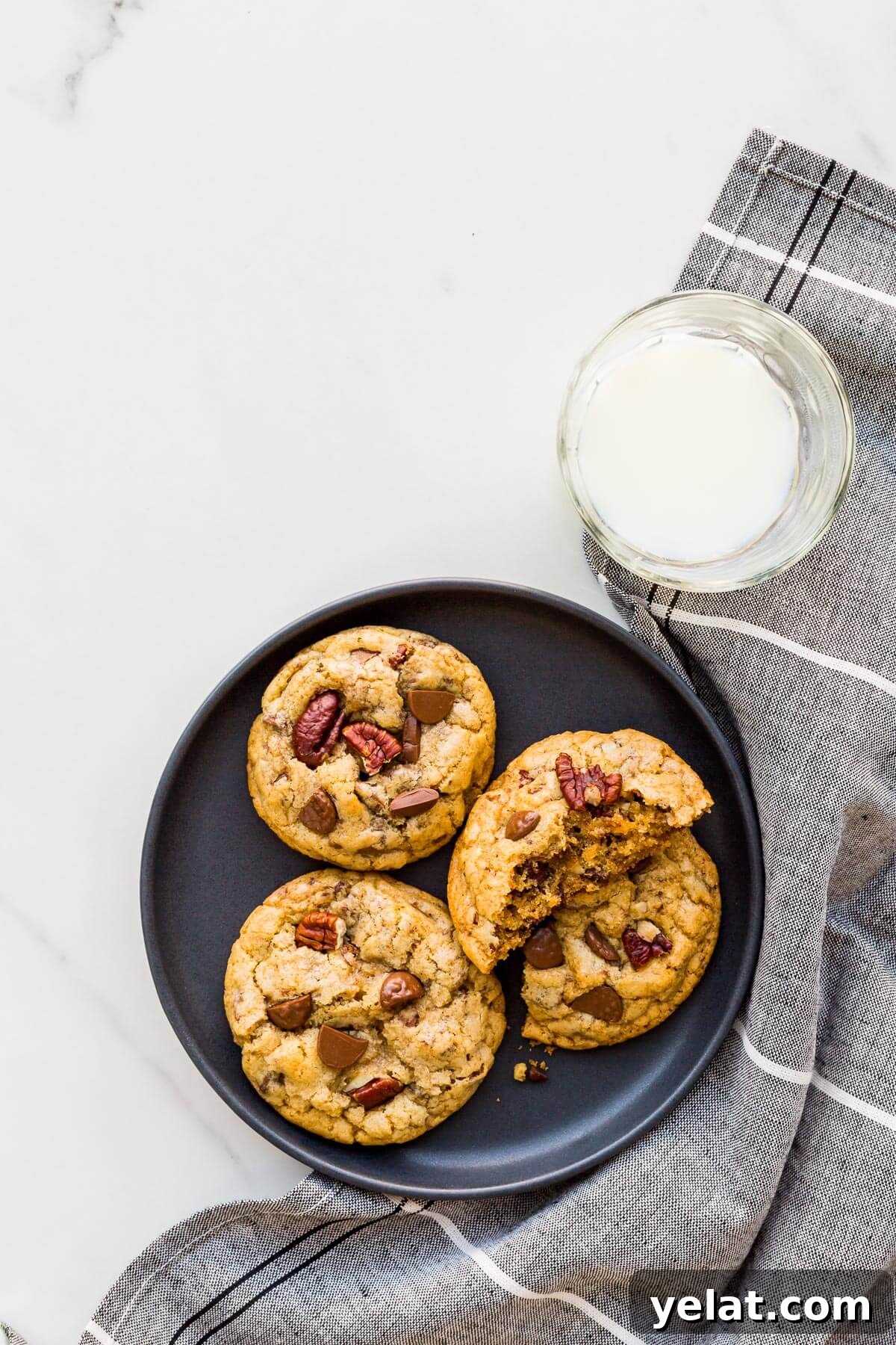 Chewy Chocolate Chip Pecan Cookies Recipe 11 Chocolate chip cookies with pecans and chunks of milk chocolate on a black plate served with a glass of milk.