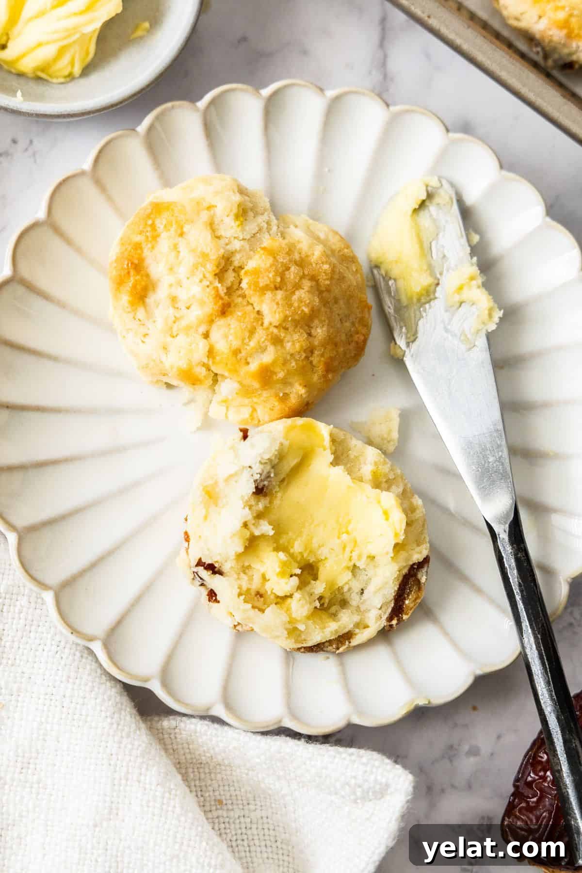Round plate with a Date and Lemon Scone cut in half, with a knife and some butter on the edge.
