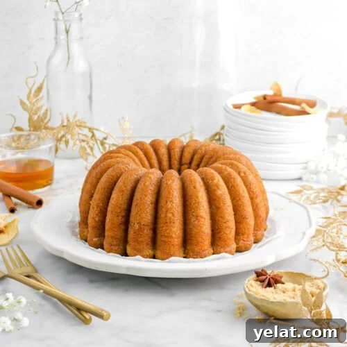 Spiced Apple Cider Bourbon Bundt Cake Recipe for Fall Desserts 14 apple bundt cake on plate with gold leaf garand around, two gold forks, and gold bowl of brown sugar beside with glass of bourbon behind.