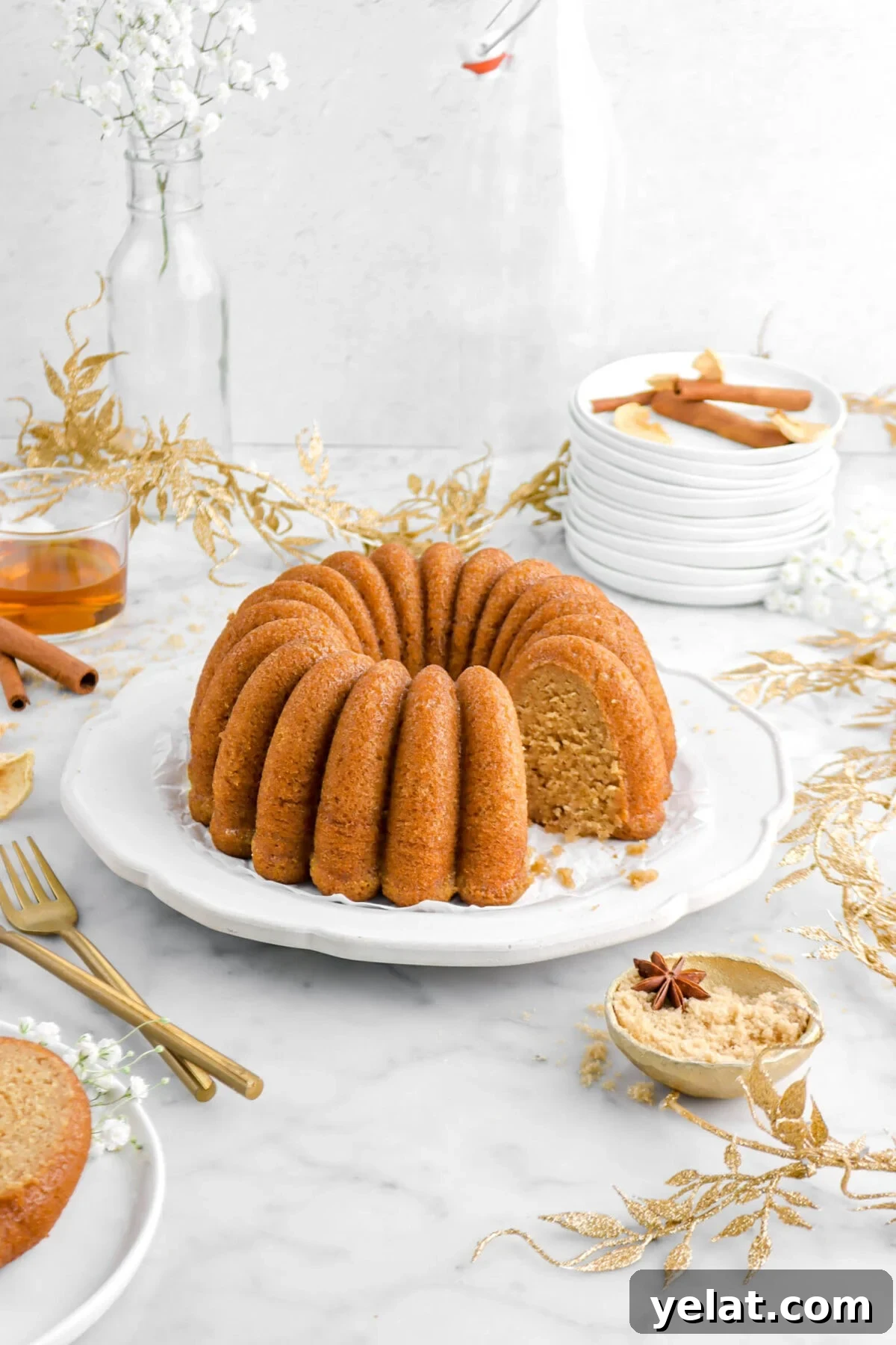 Spiced Apple Cider Bourbon Bundt Cake Recipe for Fall Desserts 4 apple cider bundt cake on plate with slices missing with forks and bowl beside, garland around, and glass of bourbon