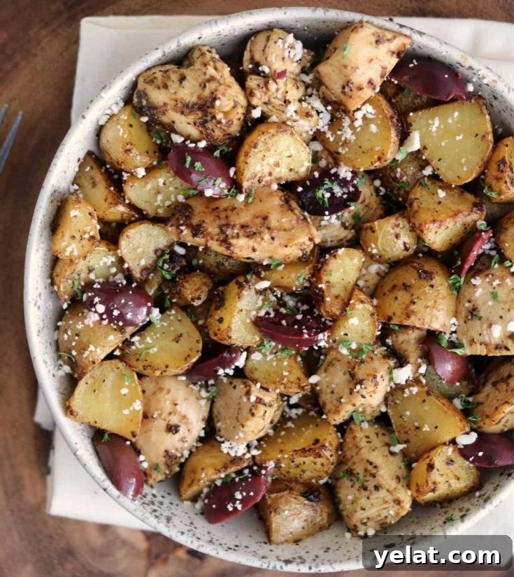 Bowl of Greek-style chicken and potatoes garnished with olives and feta.