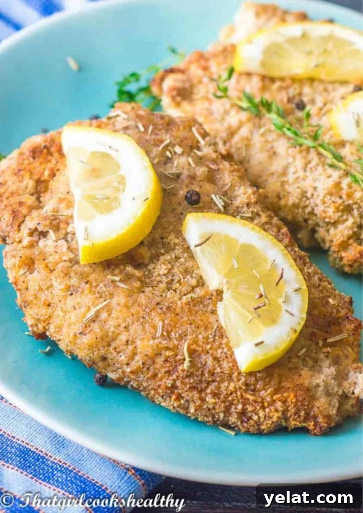 Two lemon-pepper chicken breasts on a turquoise plate garnished with lemon slices.