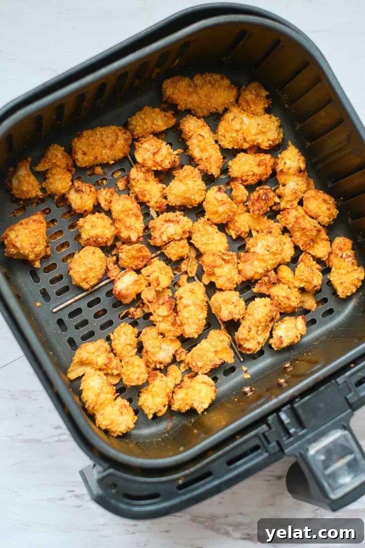 Basket-style air fryer with a batch of popcorn chicken inside.