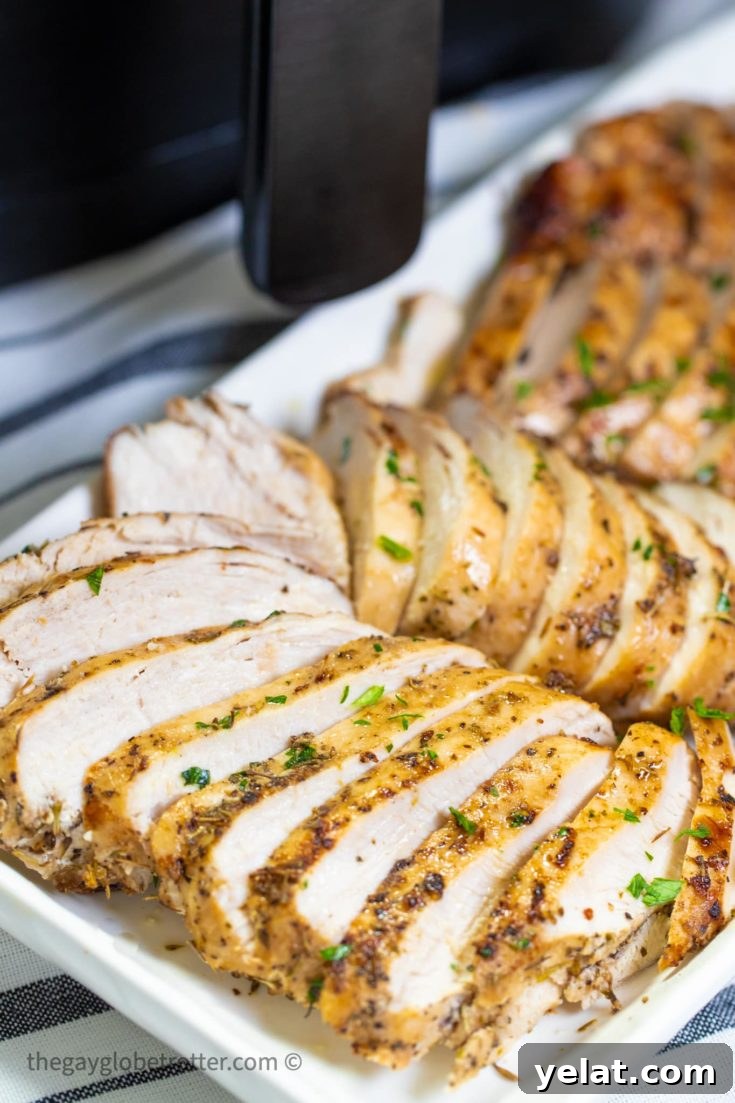 Several finished chicken breasts on a white platter with an air fryer in the background.