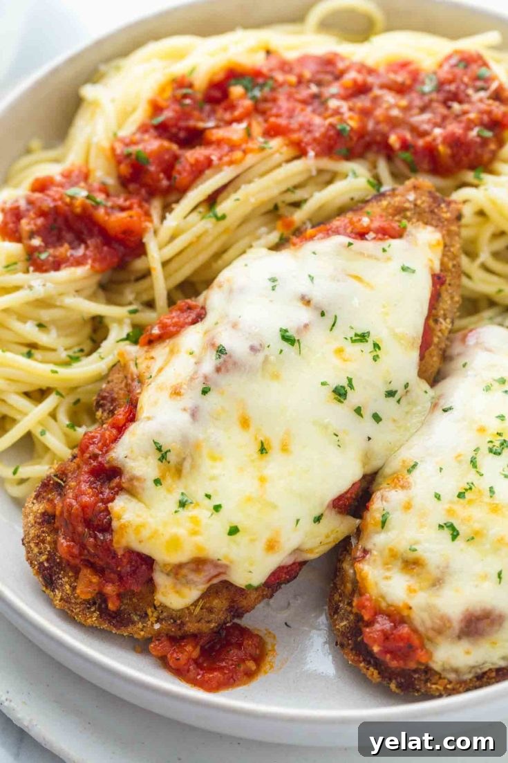 Two breaded air fried chicken breasts topped with marinara and melted mozzarella next to a side of spaghetti.
