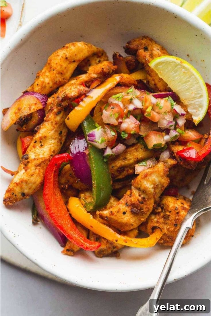 A bowl with a serving of chicken fajitas served with pico de gallo and a lime wedge.