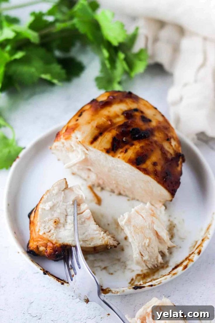 One finished chicken breast on a plate partially cut into pieces showing the interior.